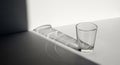 A clear glass tumbler casting a long, intricate shadow with light refractions on a stark white background Royalty Free Stock Photo