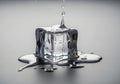 A clear ice cube with water splashing around it on a gray surface Royalty Free Stock Photo