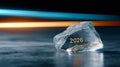 Close-up of a transparent ice cube with the year 2026 engraved inside, placed on a reflective surface with blue and orange light Royalty Free Stock Photo