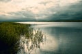 Clear lake with green plants, thick dark clouds, the sunset breaks.