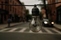 Hanging light bulb in urban street on a cloudy day with pedestrians and cars nearby Royalty Free Stock Photo