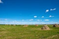 A clear sky with fluffy clouds over a green field with multiple hay piles scattered evenly Royalty Free Stock Photo