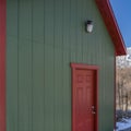 Clear Square Exterior of a storage shed with a lamp on the green wall above the red door