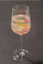 A clear sweet pink sparkling beverage decorated with fruit peels and small roses in a champagne glass.