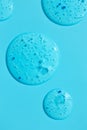 Clear transparent gel cleanser circle spots on blue, vertical macro. Cosmetic scrub texture with pilling particles. Beauty