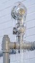 Clear Vertical Close up of a gray metal pipe covered with ice against a white brick wall Royalty Free Stock Photo