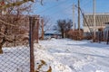 A clear view of a snow-covered piece of road, private houses, unnecessary poles and cars.