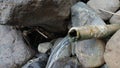 Clear water flows from a bamboo pipe among the rocks Royalty Free Stock Photo