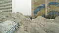 Clearing snow in the yard, traces of tire treads on the road. Huge heaps of snow on the background of multi-storey city houses on Royalty Free Stock Photo