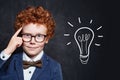 Clever boy in glasses with idea lightbulb on blackboard background