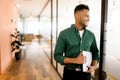 Clever elegant young indian businessman standing in modern office holding laptop