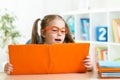 Clever kid little girl behind of open book indoor Royalty Free Stock Photo