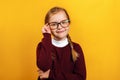 Clever little girl school girl corrects glasses. A child in a red sweater on a yellow background Royalty Free Stock Photo