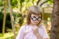 A clever smart child wearing oversized funny teacher glasses with her hand under her chin deep in thought, thinking about