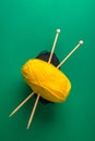 Clews of yellow black fine wool yarn crossed wooden knitting needles on dark green background warm autumn color palette. Crafts