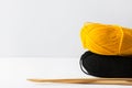 Clews of yellow black fine wool yarn wooden knitting needles on white table on wall background warm autumn color palette. Crafts