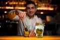 clglasses with mojito cocktail on bar counter and hand of bartender with muddler