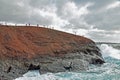 Dramatic cliff with many tourists on top and waves crashing into edge of cliff