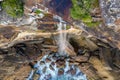 Clifftop woman sitting by the edge of waterfall tumbling into ocean