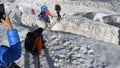 A climber crosses a large deep crack in the glacier by a metellic ladder, holding on to a rope. A long shot