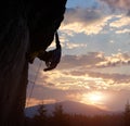 Climber holding with one hand on hanging rock at sunrise in mountains. Extreme rock climbing. Cloudy sky with copy space