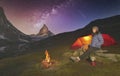 Climber resting next to the tent and fire, while preparing a hot tea, Matterhorn peak behind and the Milky Way