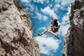 Climber teenage boy in protective helmet jumping on vertical cliff rock wall using rope Belay device, climbing harness in