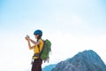 climber on top of the mountain takes a photo. Girl with a backpack and hard hat in the mountains. Woman traveler takes a photo on