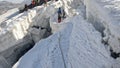 A climber walks along a narrow mountain dangerous snow-covered path past large cracks and cliffs. Trekking from Camp 2 to Camp 1