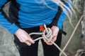 Climber woman in safety harness tying rope in bowline knot