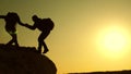 Climbers silhouettes stretch their hands to each other, climbing to the top of the hill. travelers climb one after