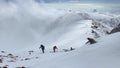 Climbers with small backpacks and trekking poles are walking on a snowy slope. Walk above the clouds. A group of tourists climbs