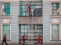 Climbers with stairs wash windows in building. Workers in branded overalls and special equipment for high-altitude work