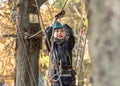 Climbing adventure park - little boy walking a track high up in the trees secured by safety equipment. Brave young child