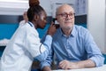 Clinic otology specialist consulting senior patient using otoscope to check ear infection