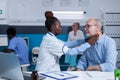 Clinic specialised otologist examining senior man while touching his neck.