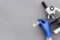 Clinical science research with microscope. Hand holds blood sample on grey background top view copy space