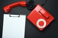 A clipboard with a blank paper next to a red vintage landline phone on a black background. Place for text. Royalty Free Stock Photo