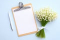 Clipboard with blank paper note, pen, bouquet of flowers lily of the valley on blue background. Flat lay, top view. Wedding Royalty Free Stock Photo