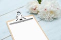 Clipboard blank sheet of paper and peony flowers on blue wooden table. Flat lay, top view. Wedding planner, checklist, to do list Royalty Free Stock Photo