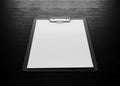 Clipboard with an empty sheet of paper on black wood background.