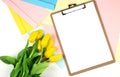 Clipboard mock up with beautiful yellow tulips with colorful envelope on white background. top view