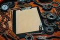 Clipboard with paper in the center of tools, gears on old metal background. Motorcycle tools, equipment and repair