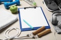 Clipboard with paper sheet, pen and sports equipment on beige table. Personal training