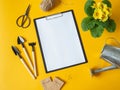 Clipboard and paper for text, yellow primrose flower, garden tools and seeds in paper bags on a yellow background. Top view Royalty Free Stock Photo