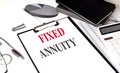 Clipboard with the text fixed annuity on a desk with financial charts, calculator, notebook, and pen Royalty Free Stock Photo