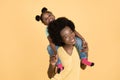 Close up horizontal shot of happy African mother, piggybacking her cute little daughter and smiling at camera. Family Royalty Free Stock Photo