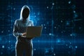 A cloaked hacker with laptop in front of a complex cyber network interface