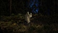 Cloaked mysterious figure stands among ferns in the forest, holding an old fashioned lantern in the dusk. 3d render Royalty Free Stock Photo