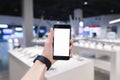 clock hand holds a phone with a white screen against the background of an electronics store